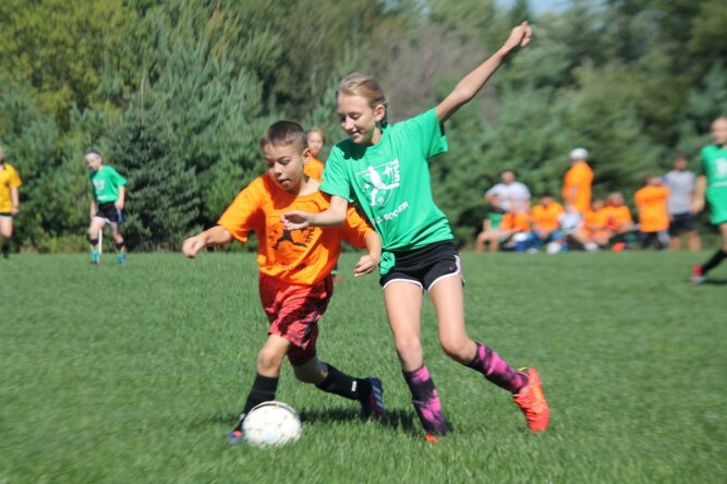 Ein Mädchen und ein Junge kämpfen auf dem Fußballfeld um den Ball.